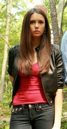 a woman standing in the woods with her hand on her hip and wearing a leather jacket