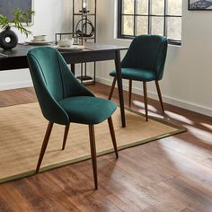 two blue chairs sitting on top of a wooden floor next to a table with a vase