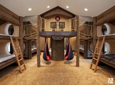 a room with bunk beds and ladders on the floor in front of it is a spiral staircase that leads up to two sets of round windows