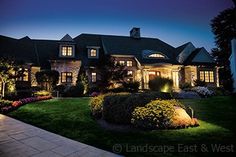 a large house lit up at night with lights on the windows and landscaping around it