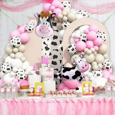 a table topped with lots of pink and white balloons next to a cow balloon wall