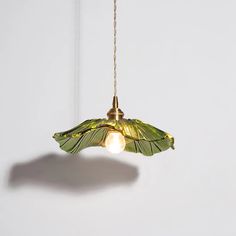 a green lamp hanging from a chain on a white wall with a light bulb in the shape of a butterfly