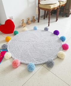 a crocheted rug with pom - poms on the floor next to two chairs