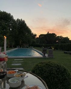 a table with food and wine on it in front of a swimming pool at sunset