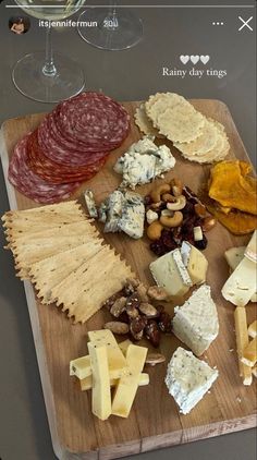 a wooden cutting board topped with lots of different types of cheese and crackers next to wine glasses