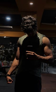 a man standing in a gym looking at his cell phone while wearing a sleeveless shirt