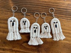 four white key chains with black eyes and fringes hanging from them on a wooden surface