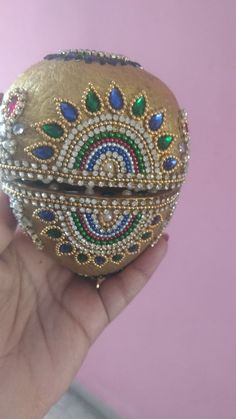 a hand holding an ornament in the shape of a ball with jewels on it