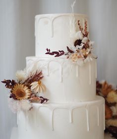 a three tiered white wedding cake with dried flowers on the side and dripping icing