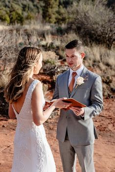 a bride and groom standing in the desert holding hands during their wedding ceremony, looking at each other