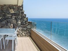 an outdoor table and chairs on a balcony overlooking the ocean in front of a stone wall