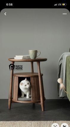 a white cat sitting in a small wooden chair next to a table with a cup on it