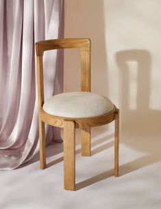 a wooden chair with a white cushion on it's seat and backrest in front of a curtained window