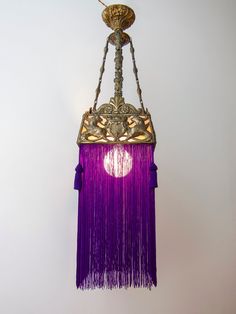 a chandelier hanging from the ceiling with purple tassels and gold accents