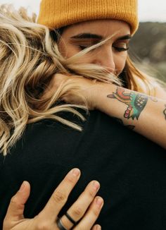 a woman with long hair and tattoos on her arm hugging another woman's shoulder