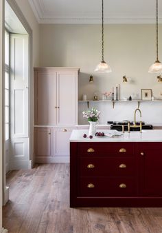 a kitchen with white and red cabinets, wood flooring and two lights hanging from the ceiling