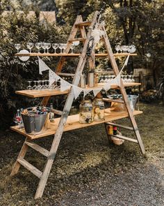 a wooden table topped with lots of bottles and glasses next to a forest filled with trees