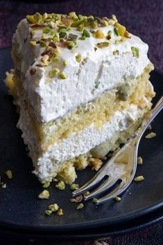 a piece of cake with white frosting and pistachio toppings on a black plate