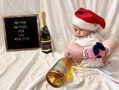 a baby wearing a santa hat sitting next to a bottle of wine and a sign