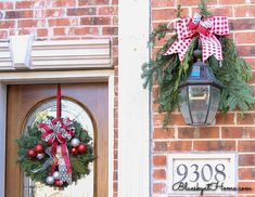 two christmas wreaths hanging on the front door of a brick building with an address plaque