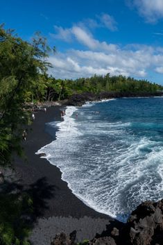 black sand beach with people swimming in the water and trees on the shore near by