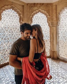 a man and woman standing in front of an ornate wall with arches on the sides