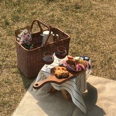 a picnic table with food and drinks on it in the grass next to a wicker basket