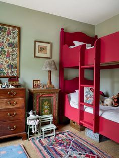 a red bunk bed sitting next to a wooden dresser and chair in a room with rugs on the floor