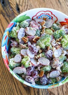 a colorful bowl filled with broccoli and other vegetables on top of a wooden table