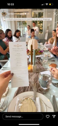 a person holding up a piece of paper at a dinner table with other people in the background