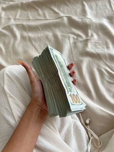 a person is laying on a bed with some money in their hand and the sheets are white