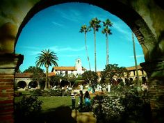 people are walking through an archway in a courtyard with palm trees on the other side