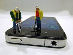 two miniature figurines are standing on top of a cell phone that is broken