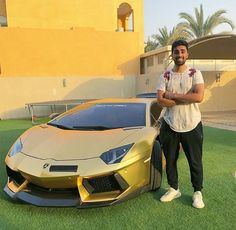 a man standing next to a gold sports car on top of a grass covered field