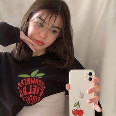 a woman is holding up her phone and looking at the camera while wearing an apple t - shirt