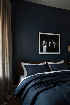 a bedroom with dark blue walls and white bedding, framed pictures on the wall