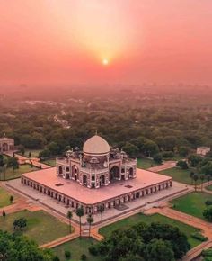 an aerial view of a large building in the middle of some trees and grass at sunset