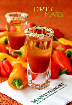 two glasses filled with liquid sitting on top of a table next to peppers and tomatoes