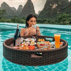 a woman sitting in a pool with food and drinks on the table next to her