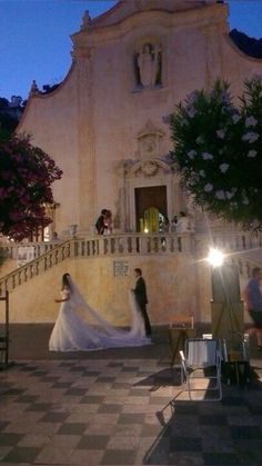 a bride and groom standing in front of a church at night with their lights on