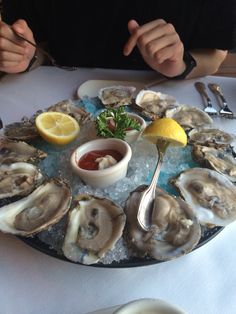 a person sitting at a table with oysters on the half shell and lemon wedges