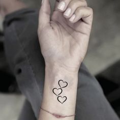 a woman's wrist tattoo with two hearts on the left side of her arm