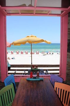 a table with an umbrella over it and some chairs on the beach in the background