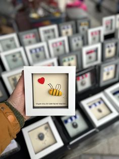 a person holding up a small card with a bee on it in front of many framed pictures