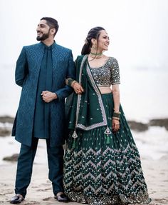 a man and woman standing next to each other on top of a sandy beach with the ocean in the background