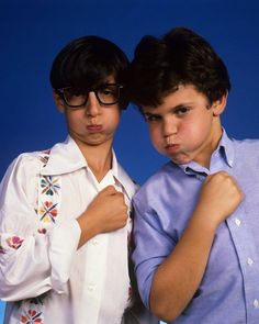 two young men standing next to each other with their arms around one another and looking at the camera