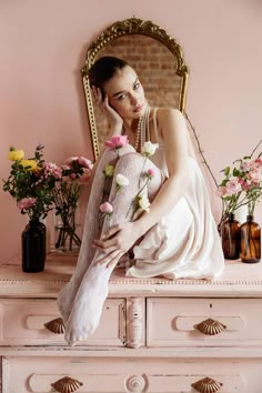 a woman is sitting on a dresser with flowers in front of her and posing for the camera