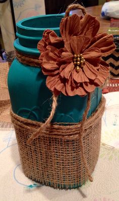 a blue mason jar with a flower on top and twine around the lid sitting on a table