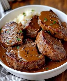 a white bowl filled with meat and gravy on top of mashed potatoes