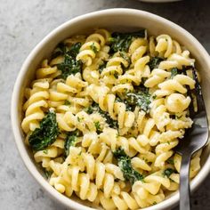 a white bowl filled with pasta and spinach on top of a gray countertop